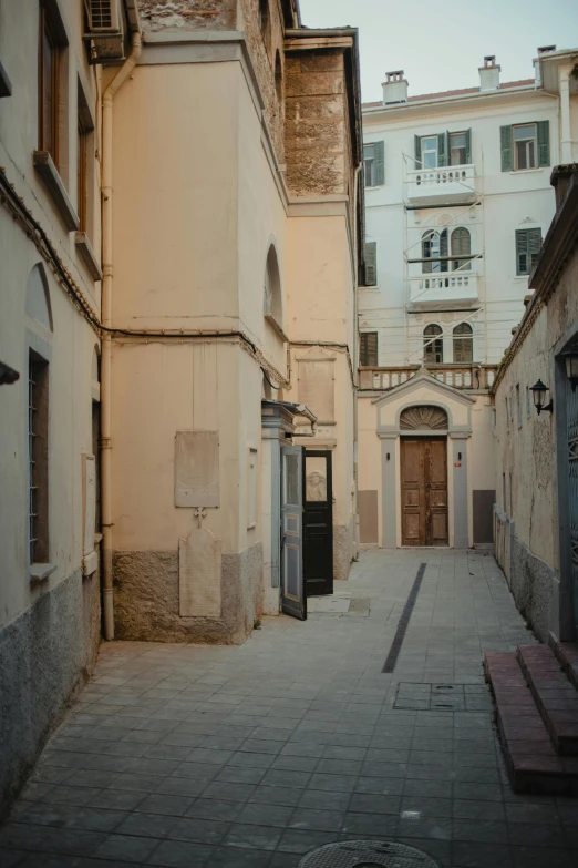 a narrow street with a bench in the middle of it, by Carlo Martini, white marble buildings, many doorways, profile image, yard