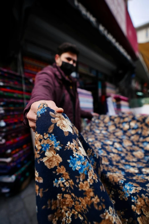 a man standing next to a pile of cloth, by Alejandro Obregón, trending on unsplash, qajar art, floral motives, photo still of behind view, made of fabric, market