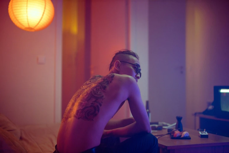 a shirtless man sitting on a bed in front of a television, a tattoo, inspired by Elsa Bleda, pexels contest winner, barely lit warm violet red light, loish |, blue and red lights, wong kar wai