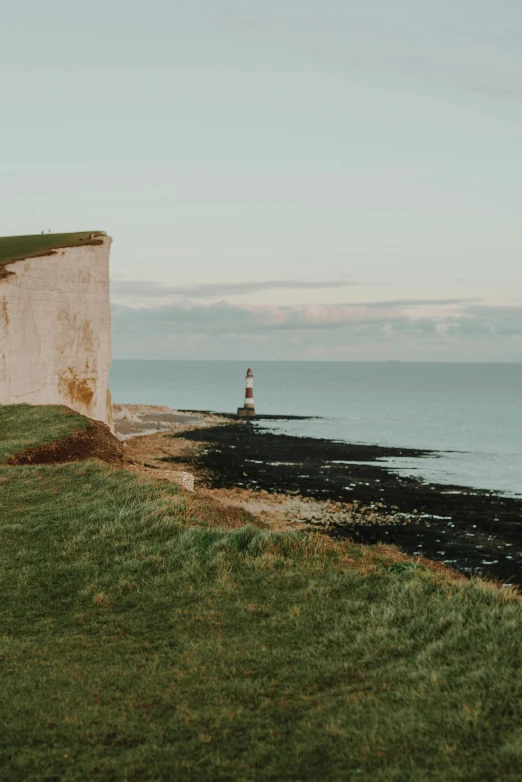 a man standing on top of a cliff next to the ocean, by David Donaldson, pexels contest winner, cliffs of dover, lighthouse in the desert, calm evening, panoramic