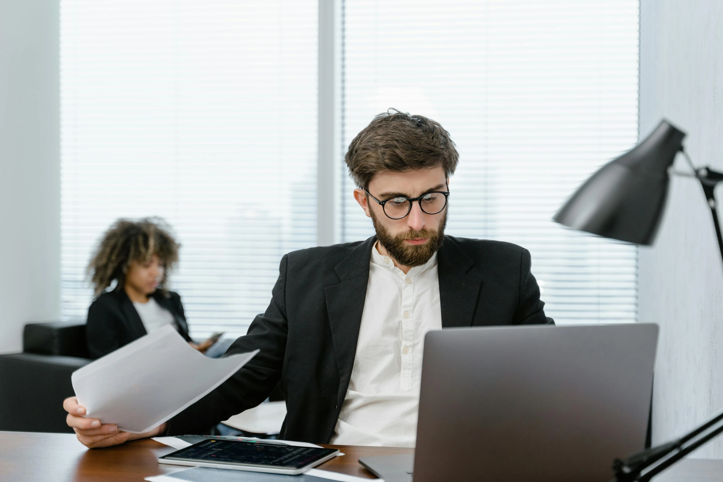 a man sitting at a table with a laptop and papers, pexels contest winner, royal commission, medium shot of two characters, open office, very professional