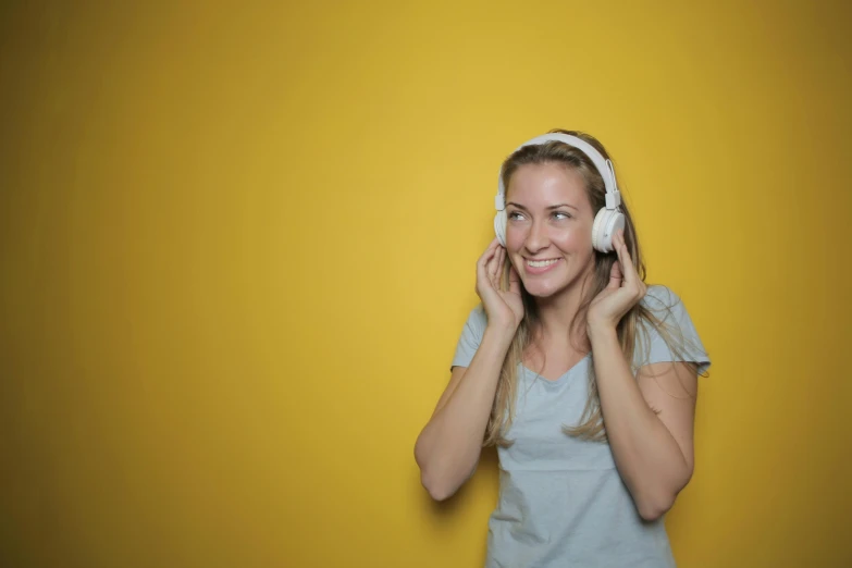 a woman holding a pair of headphones to her ear, by Adam Marczyński, trending on pixabay, yellow wallpaper, she is smiling, avatar image