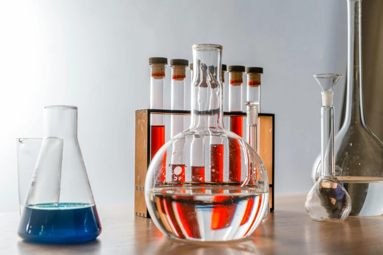a group of glass flasks sitting on top of a wooden table, trending on pexels, analytical art, blue and red, chemicals, educational display case, detailed product image