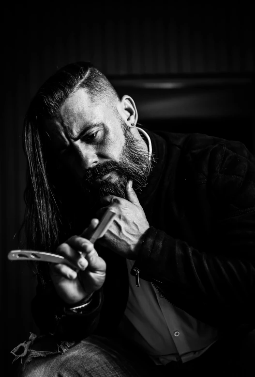 a black and white photo of a man smoking a cigarette, reddit, hyperrealism, long haircut, holding knife, long goatee beard, till lindemann