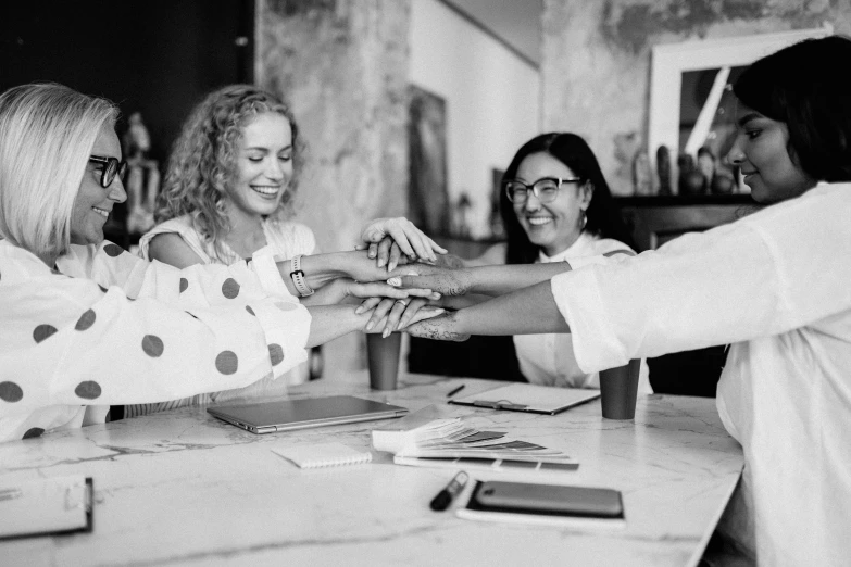 a group of women standing around a table, a black and white photo, by Emma Andijewska, pexels, big hands, happy friend, business surrounding, two women