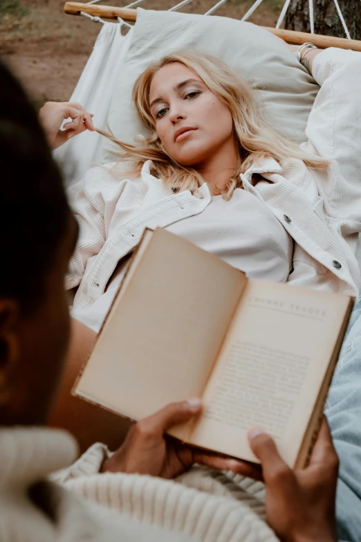 a woman laying in a hammock reading a book, a portrait, by Matija Jama, trending on pexels, romanticism, couple on bed, close up of a blonde woman, holding a giant book, concerned