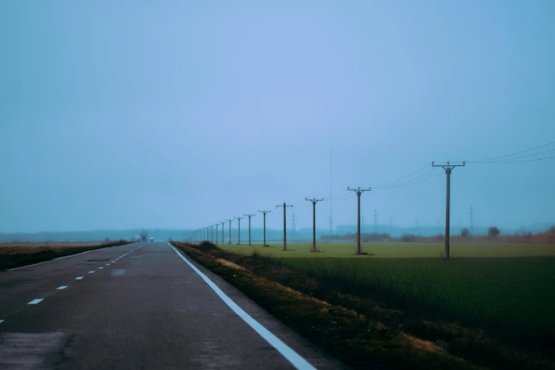 a long empty road on a foggy day, a picture, by Adam Marczyński, pexels contest winner, postminimalism, electric cables, uniform plain sky, shot on hasselblad, color photograph