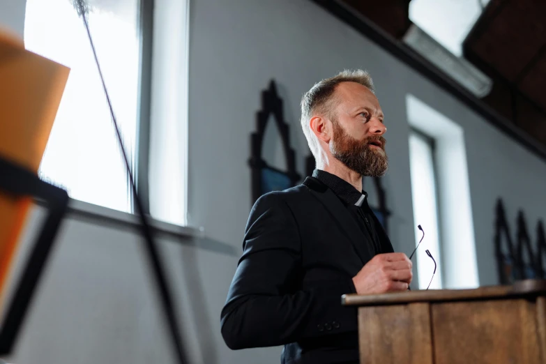 a man standing at a podium giving a speech, a portrait, by Jørgen Roed, unsplash, standing in a church, profile image, portrait image