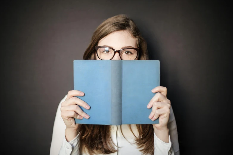 a woman holding a book in front of her face, a portrait, shutterstock, square rimmed glasses, blue, gif, small