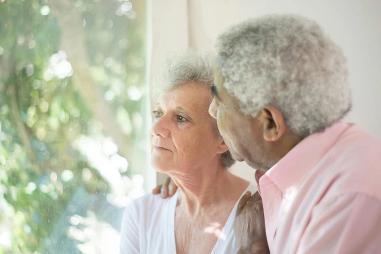 a man and a woman looking out a window, a photo, healthcare, gray haired, varying ethnicities, portrait image