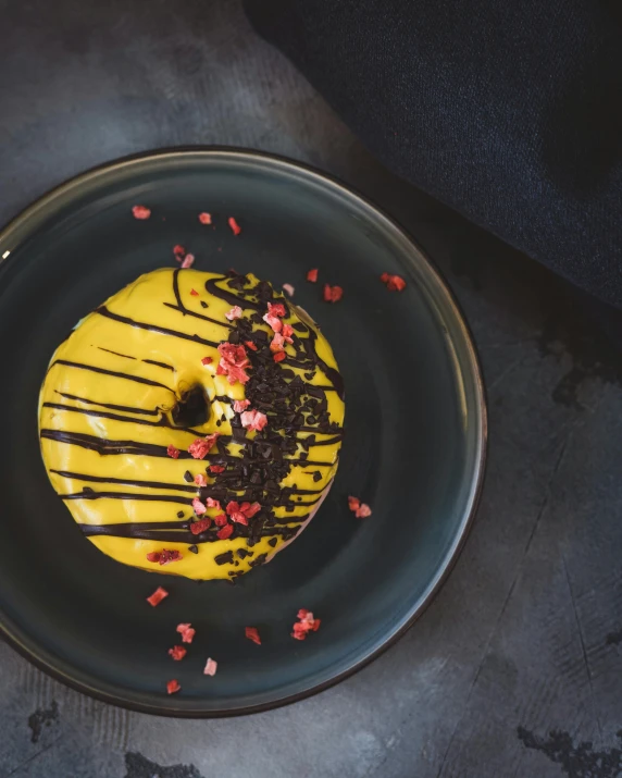 a donut sitting on top of a black plate, inspired by Barthélemy Menn, unsplash contest winner, yellow overall, vanilla smoothie explosion, beautifully painted, restaurant menu photo