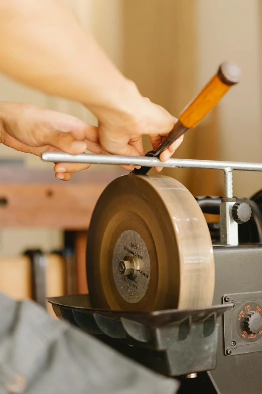 a person using a grinder to sharpe a piece of wood, inspired by Hasegawa Tōhaku, trending on pexels, arts and crafts movement, made of polished broze, holding scale and holding sword, midcentury modern, album