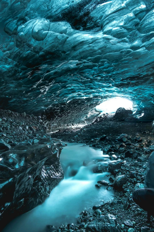 a man sitting on top of a rock next to a river, by Daarken, unsplash contest winner, in an icy cavern, inside the curl of a wave, black and cyan color scheme, lava reflections