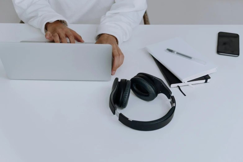 a man sitting at a table with a laptop and headphones, trending on pexels, hurufiyya, on a white table, objects, black jewellery, thumbnail