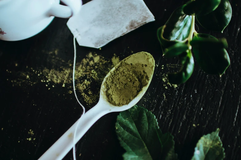 a spoon full of green tea next to a tea bag, by Julia Pishtar, trending on pexels, renaissance, dark green leaf hair, powder, multi-dimensional, poison ivy