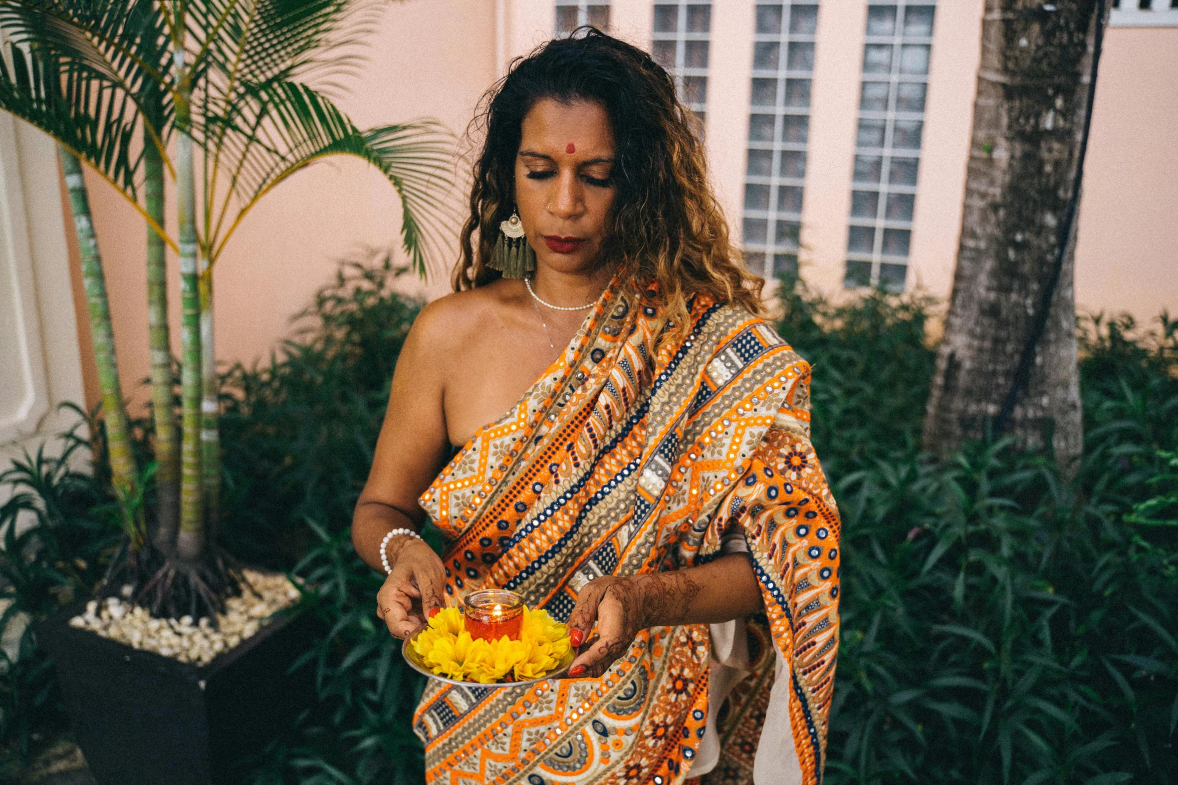 a woman in a sari holding a bowl of flowers, by Carey Morris, pexels contest winner, symbolism, white and orange breastplate, jamaica, holding a candle, indian patterns