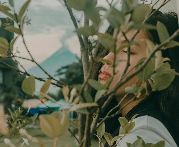 a woman standing next to a tree with her eyes closed, a picture, trending on pexels, aestheticism, cindy avelino, standing close to volcano, made of leaves, bite her lip