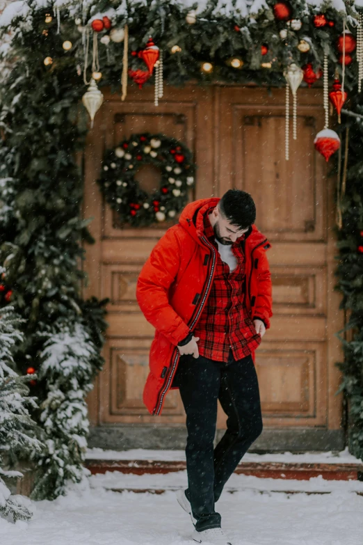 a man standing in front of a wooden door in the snow, by Julia Pishtar, pexels contest winner, wearing red jacket, holiday season, gif, tartan hoodie