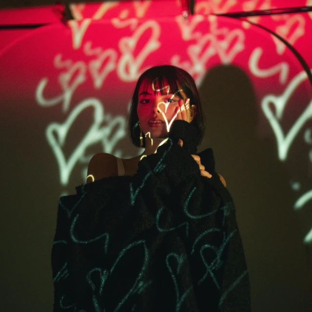 a woman holding a cell phone up to her ear, an album cover, unsplash, graffiti, vantablack cape, girl at a fashion show in hell, standing in a dimly lit room, lulu chen