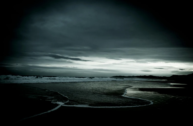 a black and white photo of the ocean, an album cover, inspired by Michal Karcz, unsplash, ominous evening, ominous, the beach, dark blue atmosphere