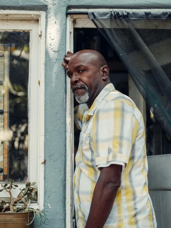 a man standing in front of a window next to a potted plant, pexels contest winner, happening, samuel jackson, in louisiana, about to enter doorframe, profile image