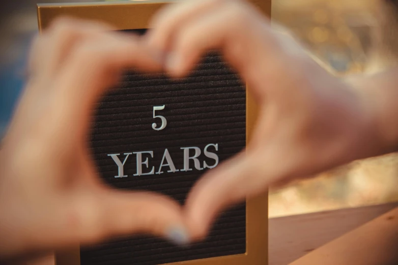 a person making a heart shape with their hands, pexels contest winner, 2 5 th anniversary music video, woman holding sign, five score years ago, on a canva