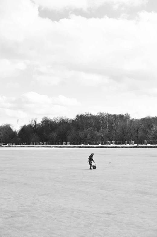 a man standing on top of a snow covered field, a black and white photo, postminimalism, riding a skateboard in berlin, picnic, the ice queen, standing on the water ground