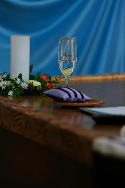 a glass of wine sitting on top of a wooden table, on the altar, blue and purple colour scheme, long table, up close