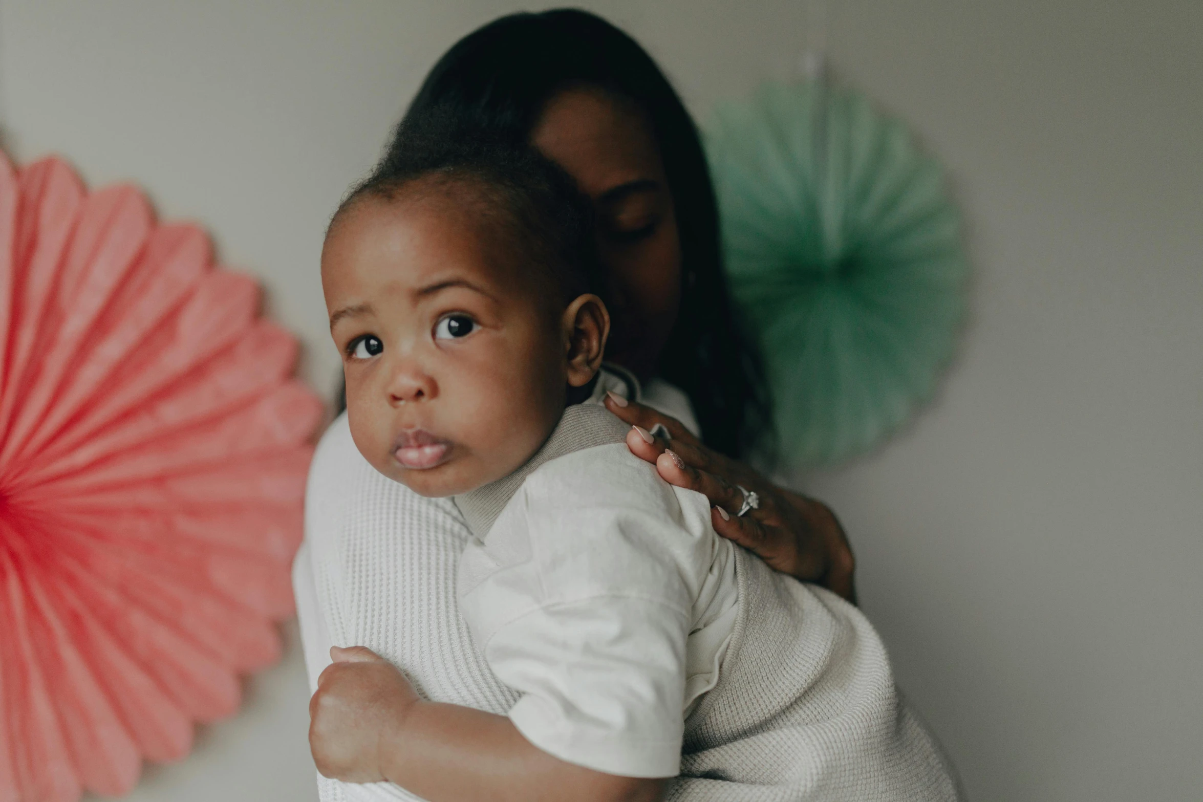 a woman holding a baby in her arms, by Arabella Rankin, pexels contest winner, mixed race, in front of white back drop, indoor picture, coloured