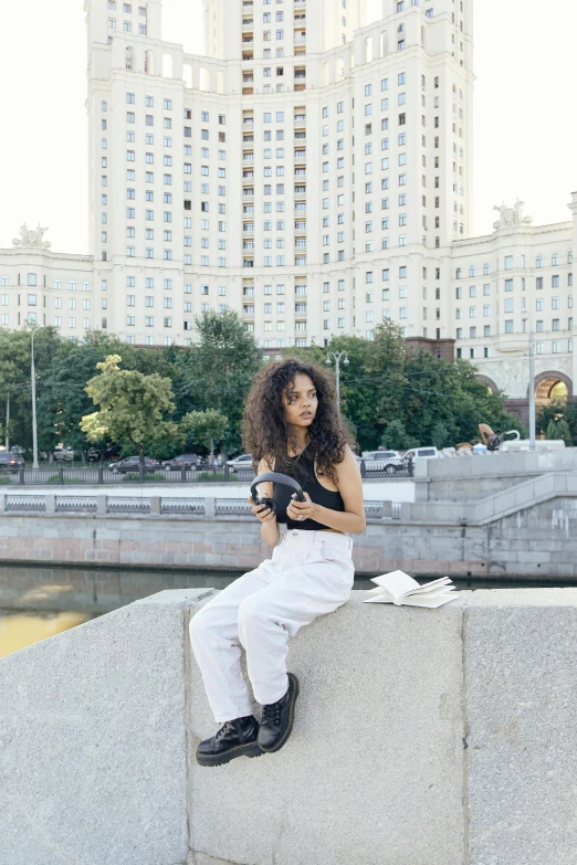 a woman sitting on a ledge reading a book, by Julia Pishtar, gta in moscow, imaan hammam, holding a camera, curls