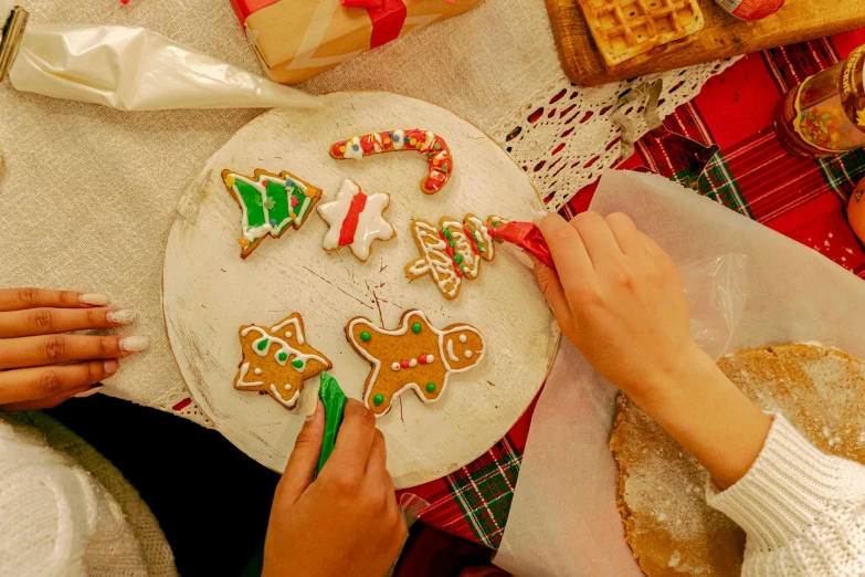 a group of people making christmas cookies on a table, by Julia Pishtar, fan favorite, unique design, ribbon, worn