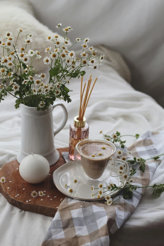 a white pitcher sitting on top of a bed next to a cup of coffee, a picture, trending on pexels, romanticism, chamomile, ✨🕌🌙, white candles, brown flowers