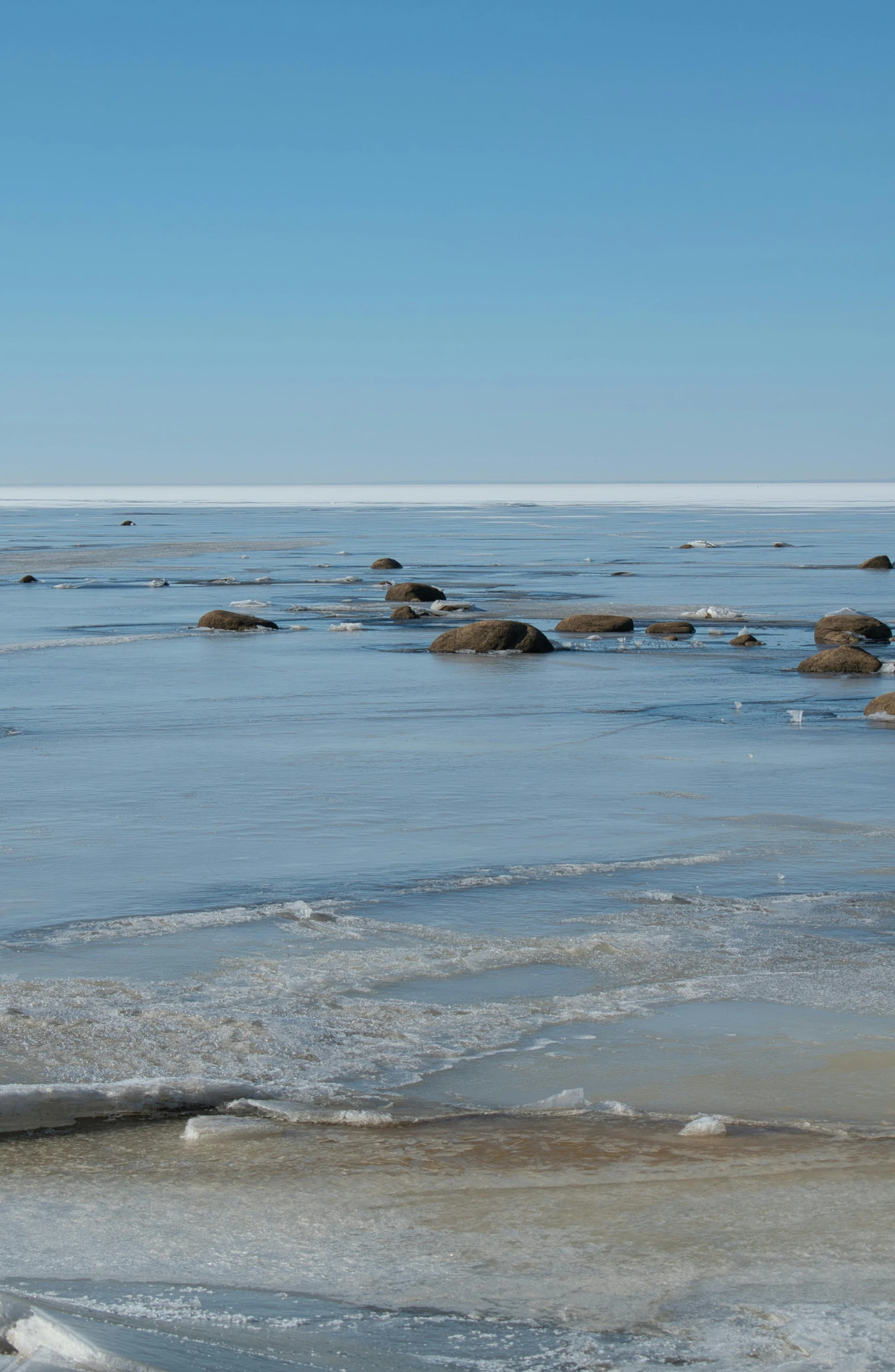 a man standing on top of a beach next to the ocean, flickr, walking across ice planet, in a row, northern finland, boulders