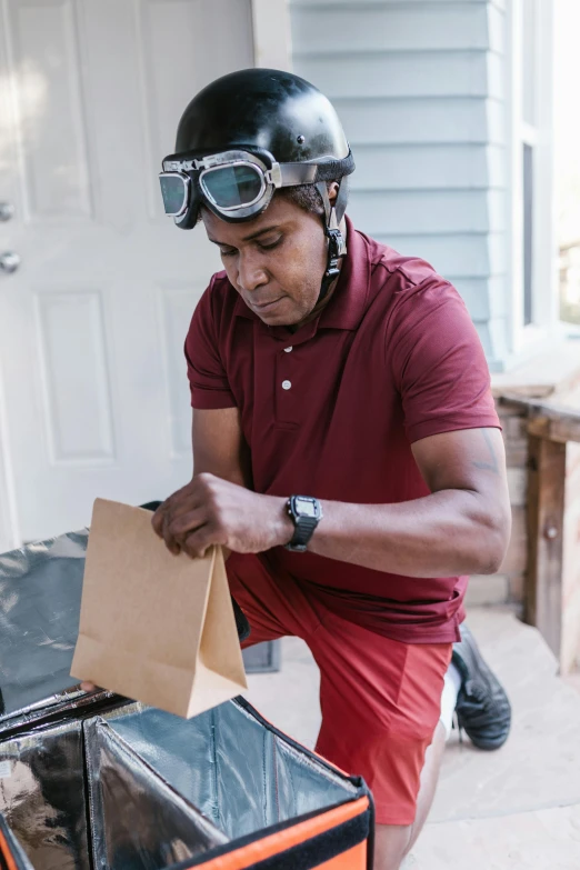 a man in a helmet and goggles working on a box, a portrait, by Ben Zoeller, pexels contest winner, carrying a saddle bag, blind brown man, standing outside a house, at checkout