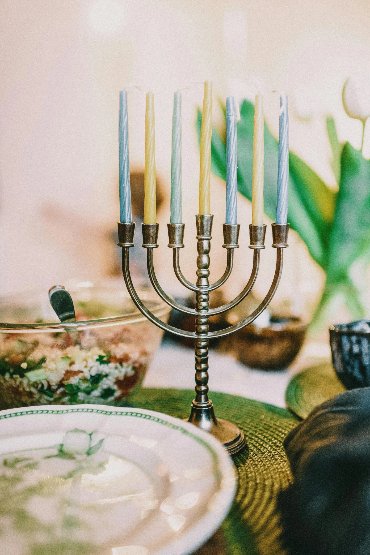 a menorah sitting on top of a table next to a plate of food, a colorized photo, trending on unsplash, green and gold, instagram story, centerpiece, table light