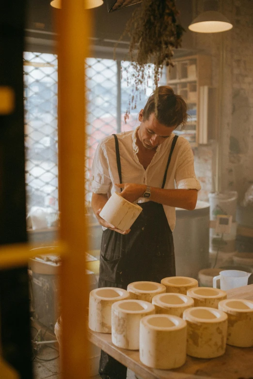 a man standing in front of a table filled with cups, a silk screen, trending on unsplash, process art, large jars on shelves, in chippendale sydney, asian man, white clay