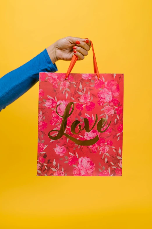 a woman holding a shopping bag with the word love on it, by Julia Pishtar, gilded. floral, red and yellow color scheme, high quality paper, 8l