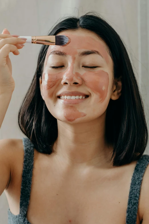 a woman brushes her face with a brush, by Julia Pishtar, smiling mask, silicone skin, asian woman, terracotta