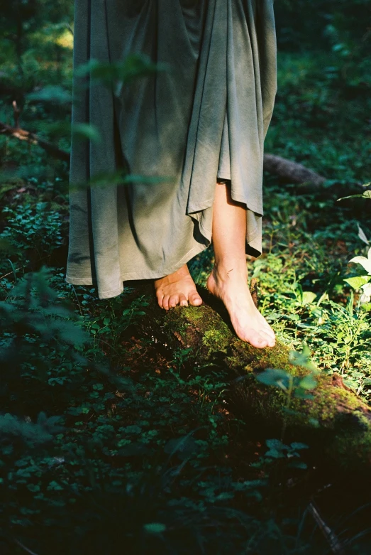 a woman standing on a log in the woods, an album cover, by Ren Hang, unsplash, renaissance, detailed foot shot, green robe, ((forest)), cottage hippie naturalist