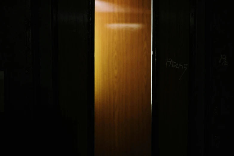 a wooden door with writing on it in a dark room, an album cover, inspired by Nan Goldin, hurufiyya, in an elevator, photographed for reuters, humongous, yellow light