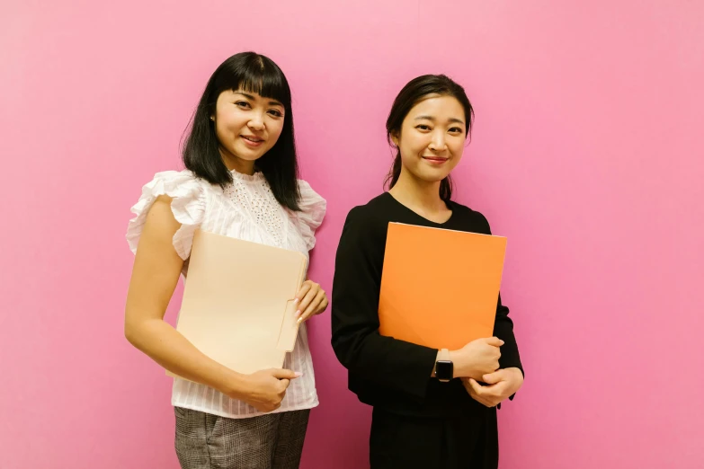 a couple of women standing next to each other, by Jang Seung-eop, pexels contest winner, academic art, pink and orange, holding a clipboard, ethnicity : japanese, office background