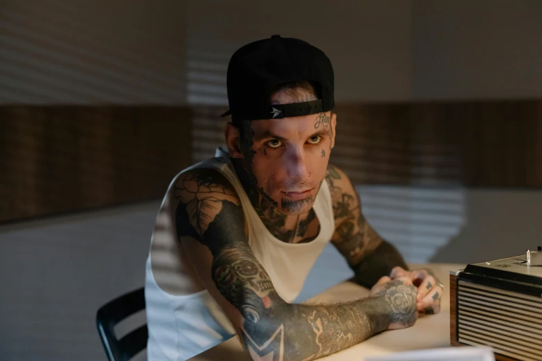 a man sitting at a table with a radio in front of him, a tattoo, inspired by Seb McKinnon, trending on pexels, hyperrealism, glare face, looking the camera, bladee from drain gang, portrait of ben stiller