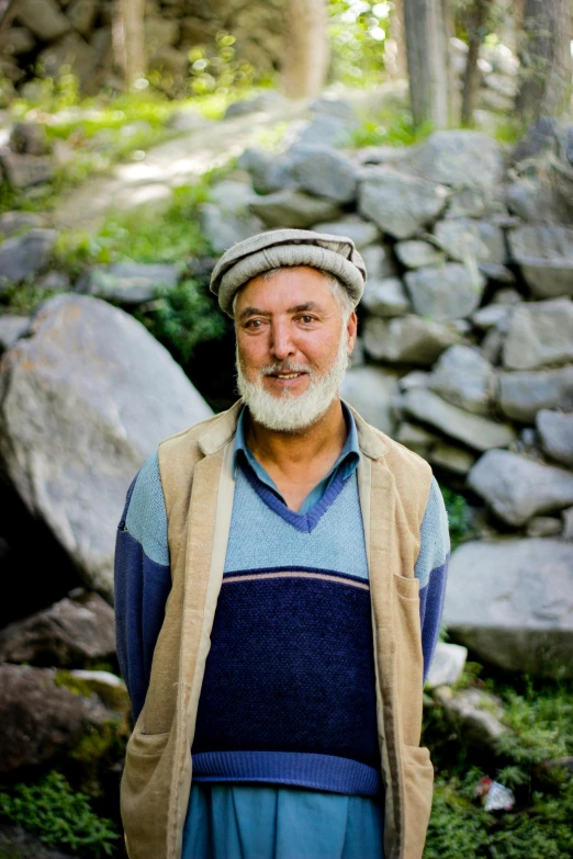a man standing in front of a pile of rocks, white hair and white beard, ismail, an afghan male type, serene smile