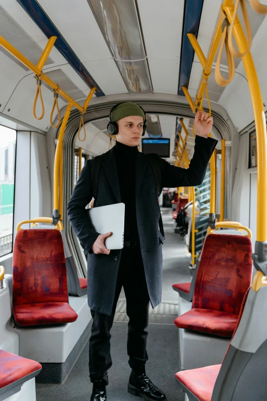 a man in a black coat standing on a train, pexels contest winner, bauhaus, wearing headset, vitalik buterin, holding a clipboard, public bus