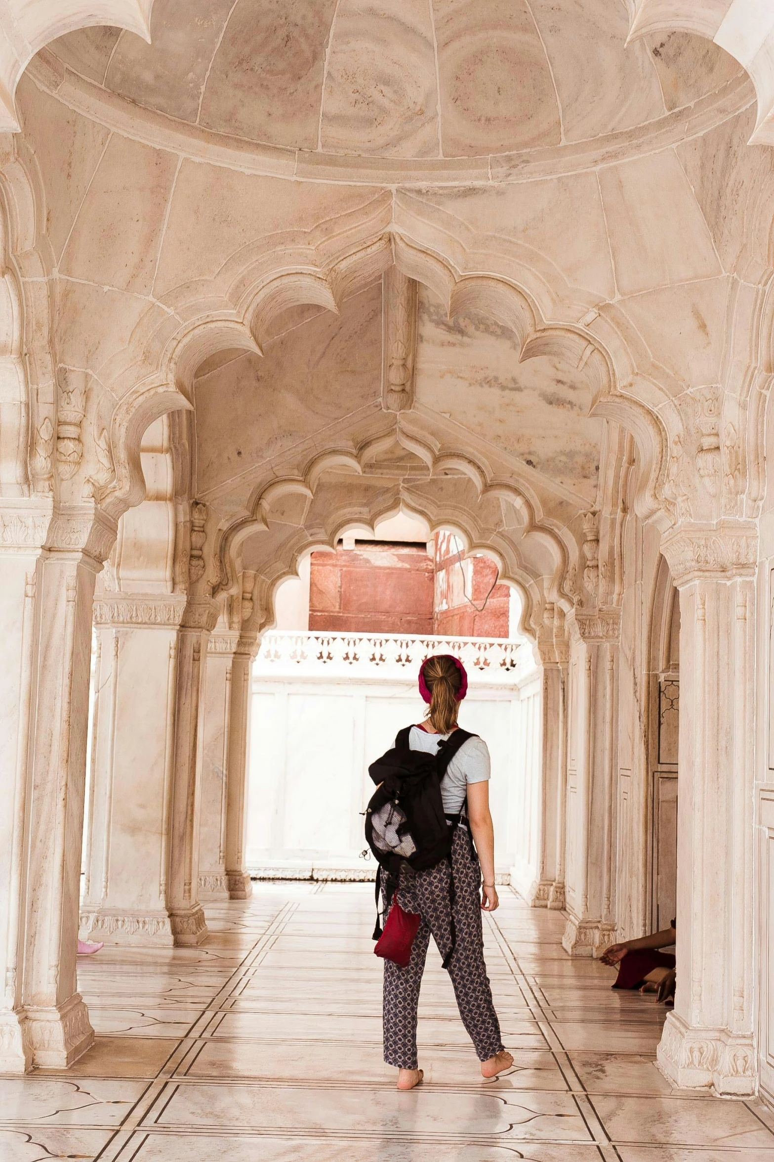 a woman with a backpack standing in a building, a marble sculpture, inspired by Steve McCurry, arabesque, white stone arches, taj mahal, maroon and white, m