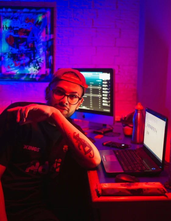 a man sitting in front of a laptop computer, an album cover, pexels contest winner, process art, bisexual lighting, sitting at a control center, low quality photo, looking straight to camera