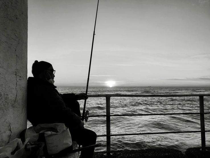 a man sitting on a bench next to the ocean, a black and white photo, pexels contest winner, realism, fishing pole, sun behind her, profile image, an oldman