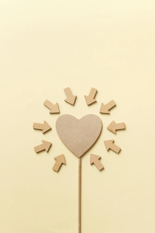 a heart shaped cake topper sitting on top of a table, inspired by karlkka, trending on unsplash, conceptual art, arrows, beige color scheme, made of cardboard, pale yellow wallpaper