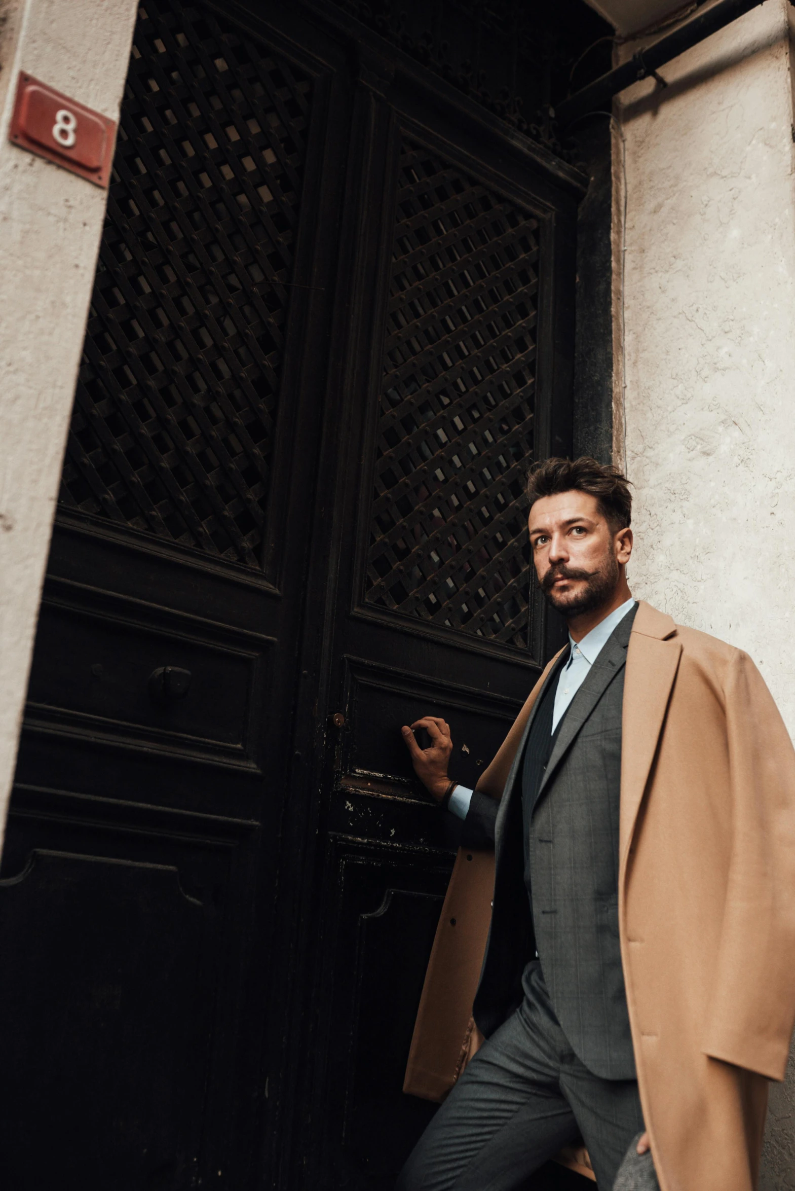 a man in a coat leaning against a door, inspired by Francesco Furini, pexels contest winner, short brown beard, tan suit, guido reni style, young spanish man