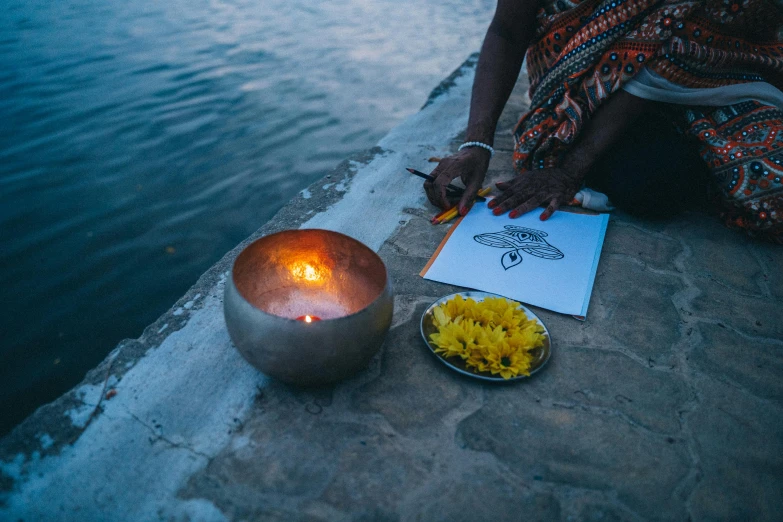 a woman sitting on the edge of a body of water next to a bowl of food and a lit candle, a picture, glowing ceremonial markings, on a canva, close - up photograph, close-up photograph